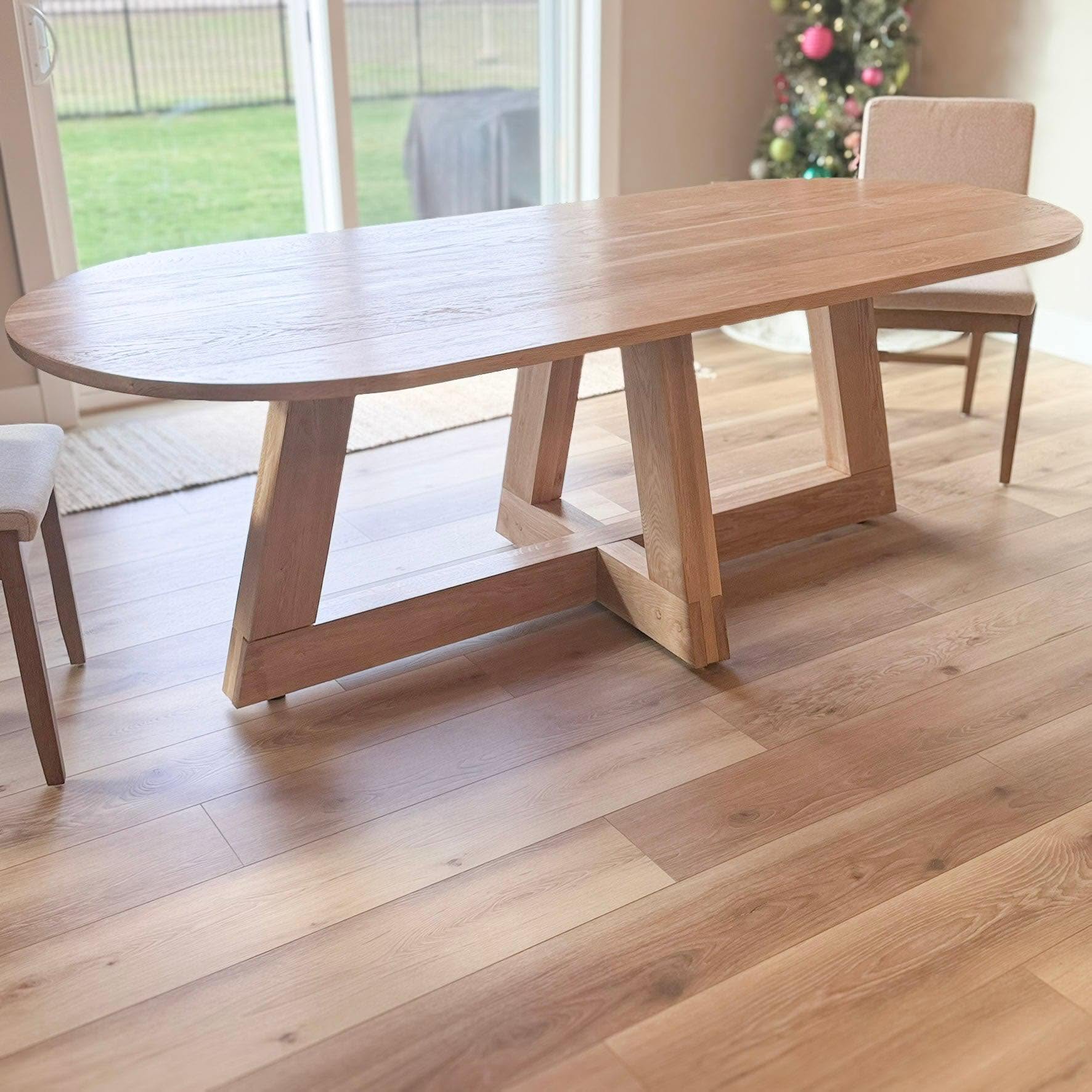 Custom oval white oak trestle dining table in a bright dining room with sliding doors to the backyard